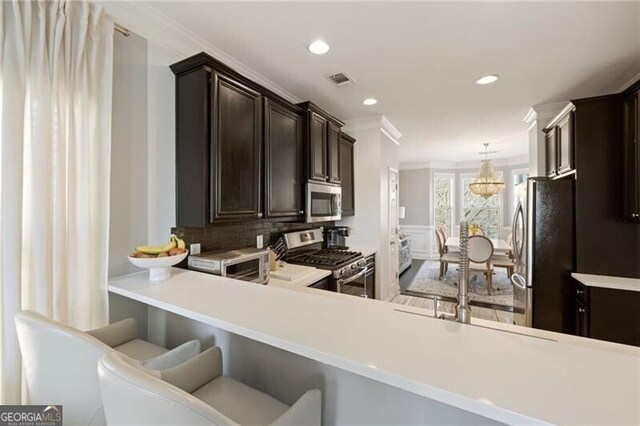 kitchen with ornamental molding, dark brown cabinetry, appliances with stainless steel finishes, light countertops, and a chandelier