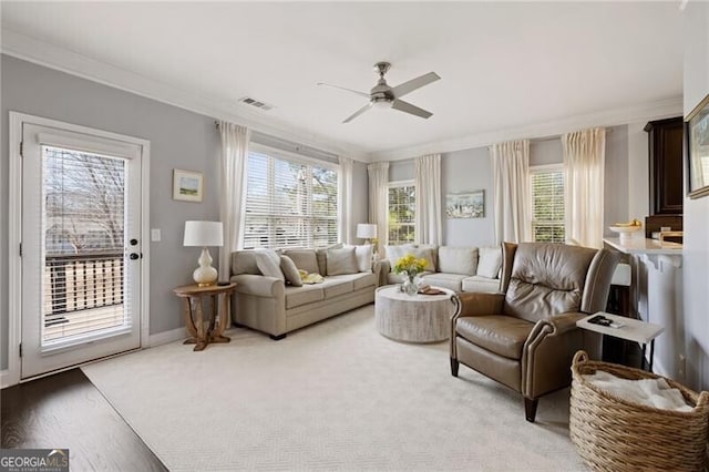 living area with crown molding, baseboards, visible vents, and ceiling fan