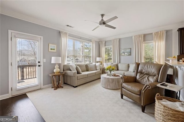 living room with visible vents, crown molding, baseboards, light wood-style flooring, and a ceiling fan