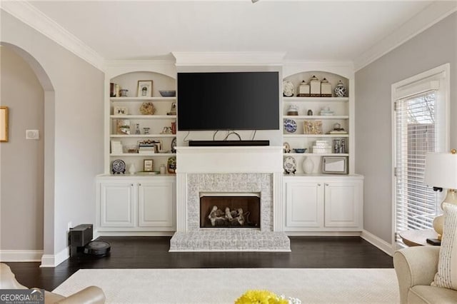 living area featuring arched walkways, built in features, dark wood-type flooring, and baseboards