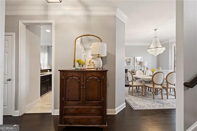 hallway with ornamental molding, baseboards, an inviting chandelier, and wood finished floors