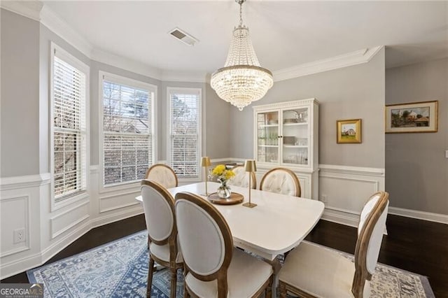 dining area featuring visible vents, crown molding, dark wood-type flooring, a chandelier, and wainscoting