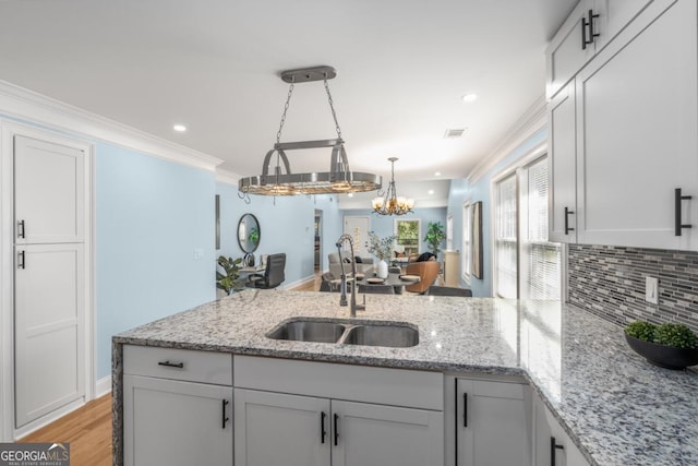 kitchen with a peninsula, ornamental molding, a sink, tasteful backsplash, and a chandelier