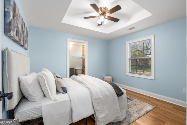 bedroom with visible vents, baseboards, a tray ceiling, and wood finished floors