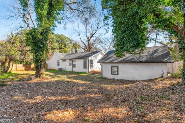 back of property with cooling unit, fence, and a shingled roof