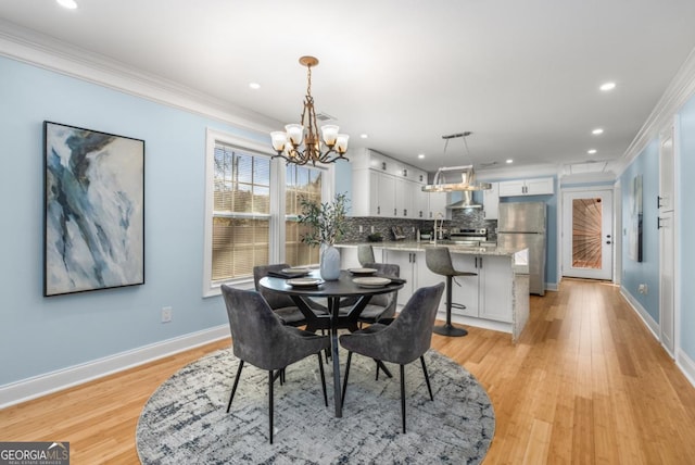 dining area featuring a notable chandelier, light wood-type flooring, crown molding, and baseboards