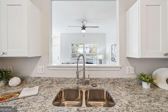 kitchen with white cabinetry, light stone counters, and a sink