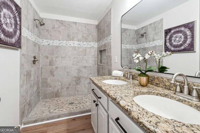 full bathroom with double vanity, wood finished floors, a tile shower, and a sink