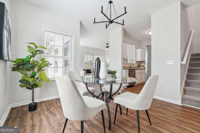 dining area featuring baseboards, wood finished floors, stairs, and ceiling fan with notable chandelier