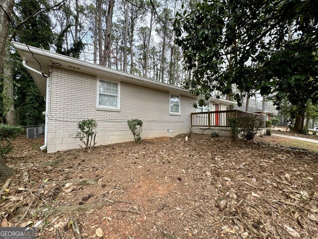 view of property exterior featuring a deck, brick siding, and crawl space