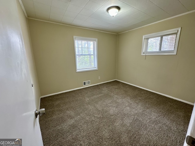 spare room with a wealth of natural light, visible vents, dark carpet, and crown molding