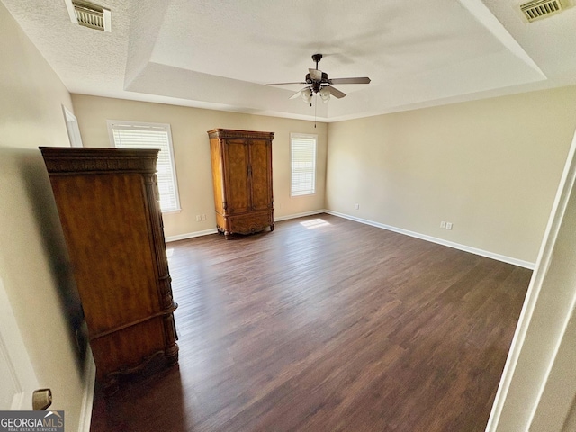 unfurnished bedroom with visible vents, a raised ceiling, baseboards, and dark wood-style flooring