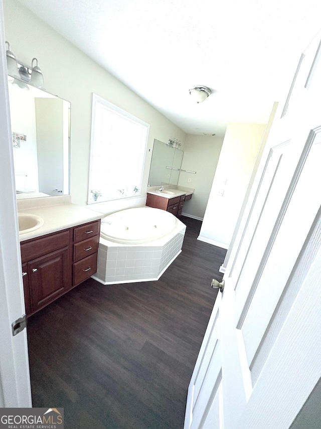 full bath with a sink, a garden tub, two vanities, and wood finished floors