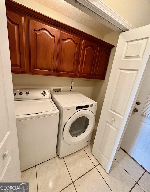 clothes washing area featuring washer and clothes dryer, light tile patterned floors, and cabinet space