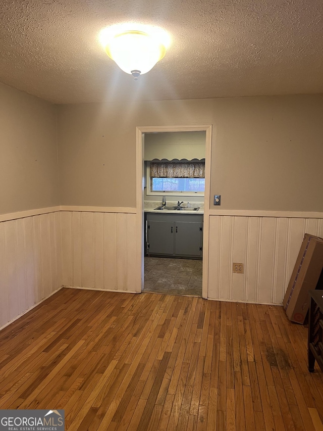 spare room featuring a sink, a wainscoted wall, a textured ceiling, and hardwood / wood-style floors