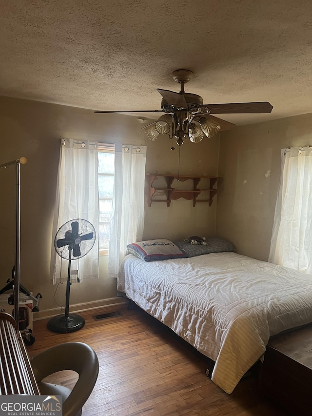 bedroom featuring a ceiling fan, wood finished floors, visible vents, and a textured ceiling