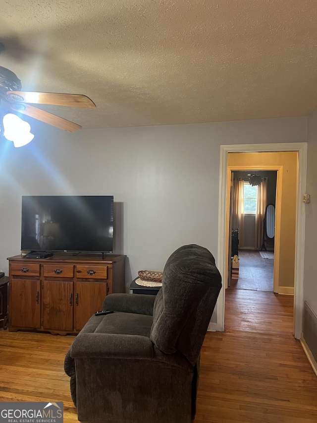 living area featuring visible vents, a textured ceiling, light wood-style flooring, and a ceiling fan