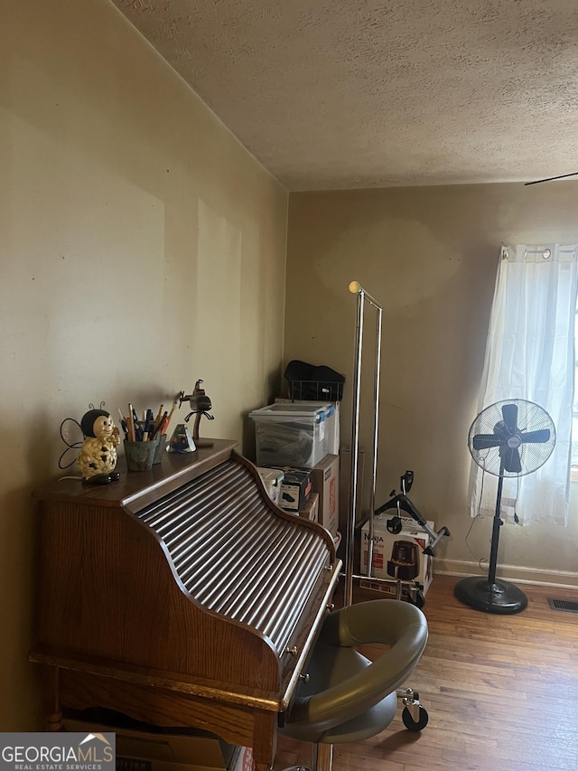 misc room featuring visible vents, a textured ceiling, baseboards, and wood finished floors