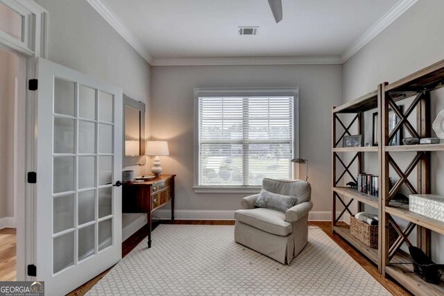 living area with wood finished floors, visible vents, baseboards, and ornamental molding