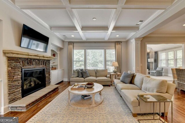 living room with wood finished floors, coffered ceiling, decorative columns, a glass covered fireplace, and beamed ceiling