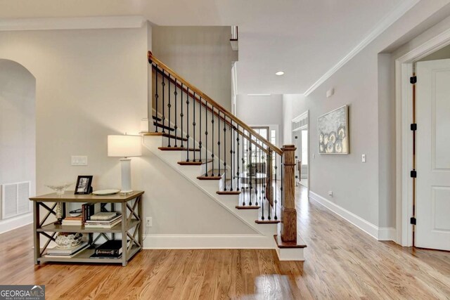 stairway featuring visible vents, baseboards, ornamental molding, wood finished floors, and arched walkways