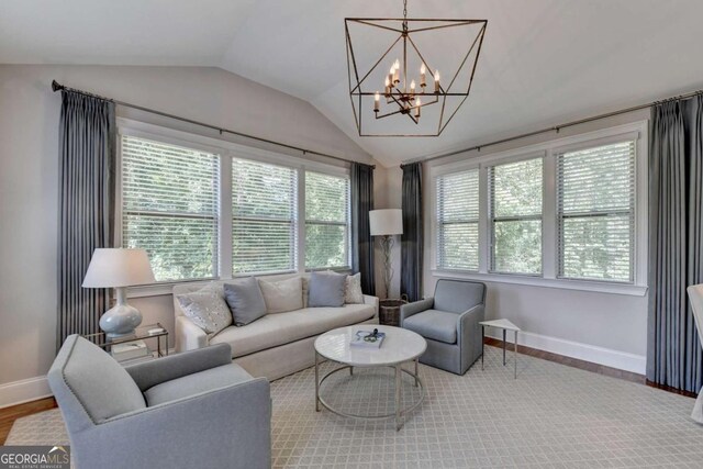 living area with a notable chandelier, wood finished floors, baseboards, and vaulted ceiling