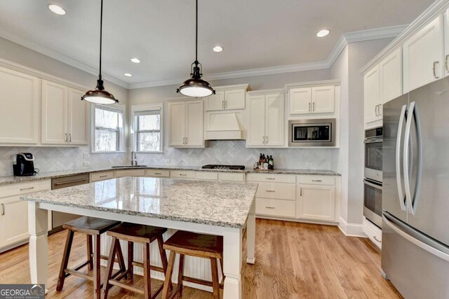 kitchen featuring appliances with stainless steel finishes, white cabinetry, light wood-type flooring, and premium range hood