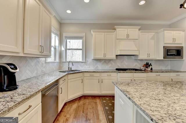 kitchen with crown molding, appliances with stainless steel finishes, light wood-style floors, custom exhaust hood, and a sink