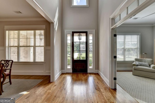 foyer entrance with wood finished floors, visible vents, a wealth of natural light, and ornamental molding