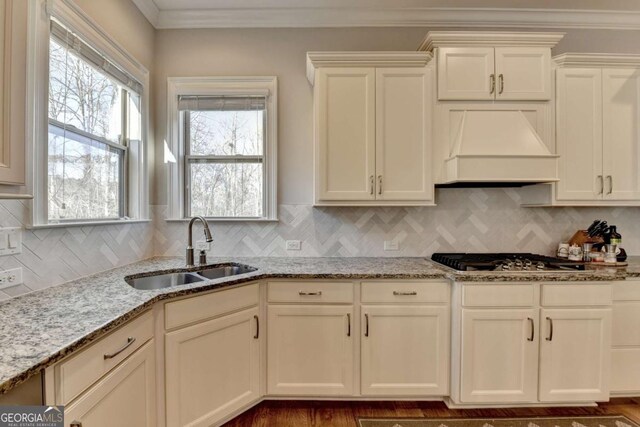 kitchen with light stone countertops, stainless steel gas cooktop, custom exhaust hood, a sink, and crown molding