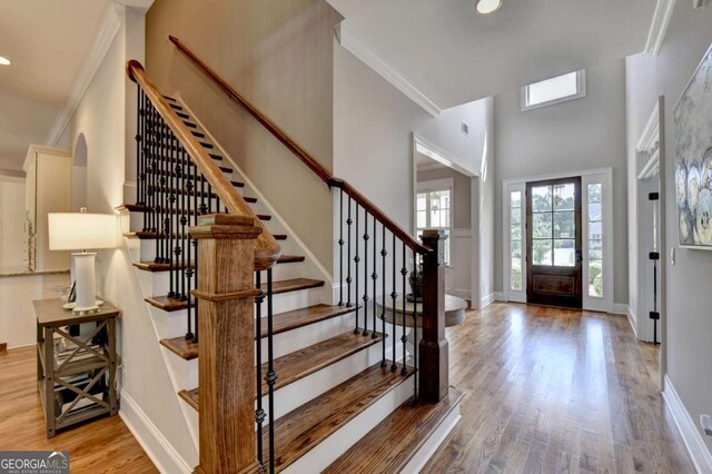 foyer with ornamental molding, baseboards, a towering ceiling, and wood finished floors