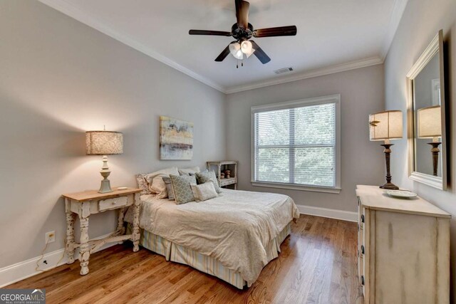 bedroom with light wood-type flooring, visible vents, ornamental molding, baseboards, and ceiling fan