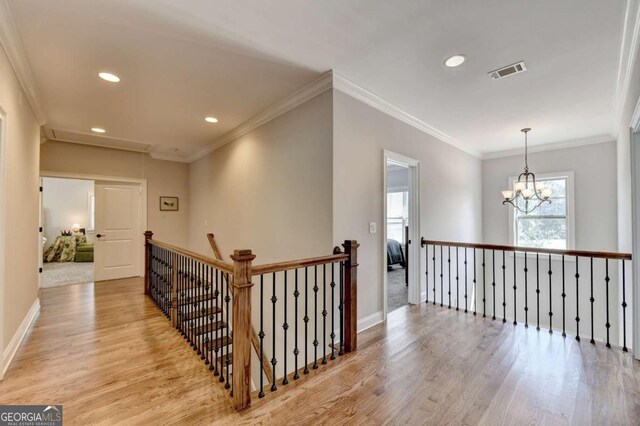 corridor with light wood-type flooring, visible vents, an upstairs landing, and attic access