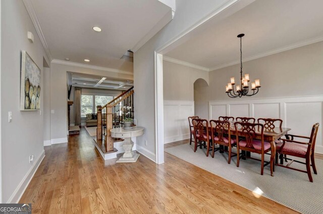 dining area with a wainscoted wall, stairs, ornamental molding, wood finished floors, and a notable chandelier