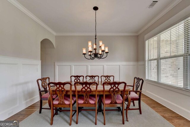 dining space featuring visible vents, arched walkways, a notable chandelier, and wood finished floors