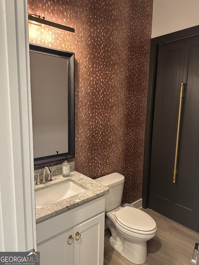 bathroom featuring vanity, toilet, wood finished floors, and wallpapered walls