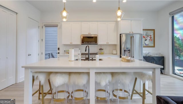 kitchen with a sink, stainless steel appliances, light countertops, white cabinetry, and backsplash