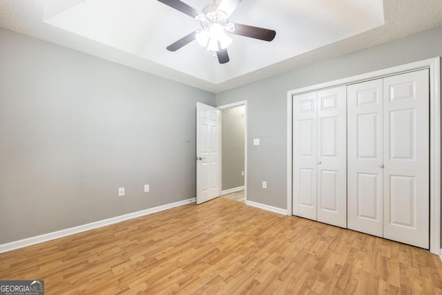 unfurnished bedroom with a ceiling fan, baseboards, a tray ceiling, a closet, and light wood-type flooring