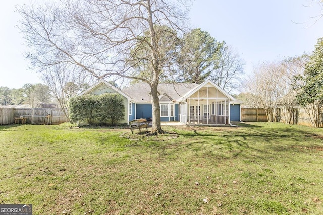 rear view of house featuring a lawn, a fenced backyard, and a sunroom