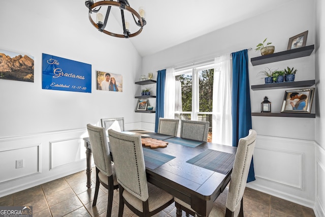 tiled dining space featuring a decorative wall, wainscoting, an inviting chandelier, and lofted ceiling