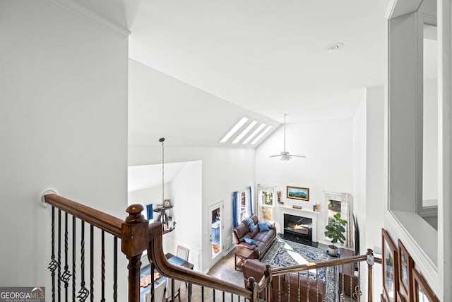 stairway featuring a premium fireplace, high vaulted ceiling, a skylight, and ceiling fan with notable chandelier