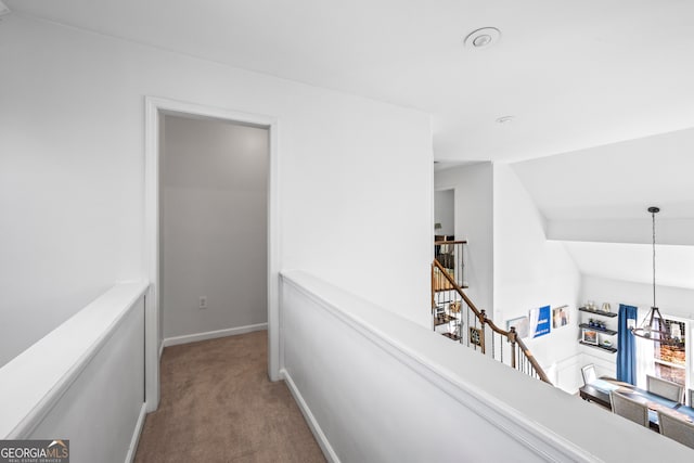 hallway featuring carpet, baseboards, an inviting chandelier, lofted ceiling, and an upstairs landing