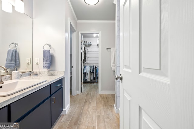 bathroom with vanity, wood finished floors, baseboards, ornamental molding, and a walk in closet