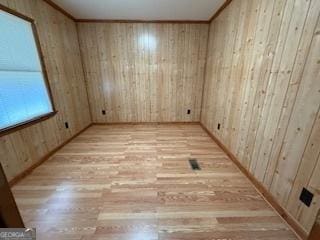 empty room featuring wooden walls, crown molding, and light wood-type flooring