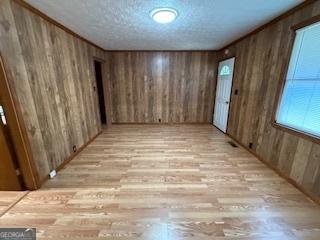 unfurnished room with light wood-type flooring, wooden walls, and a textured ceiling