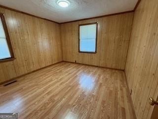 empty room featuring wooden walls, visible vents, ornamental molding, wood finished floors, and a textured ceiling