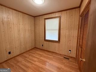 unfurnished room featuring crown molding, wooden walls, and wood finished floors