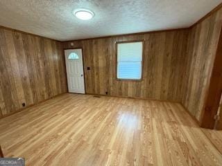 empty room with light wood-type flooring, a textured ceiling, and wood walls