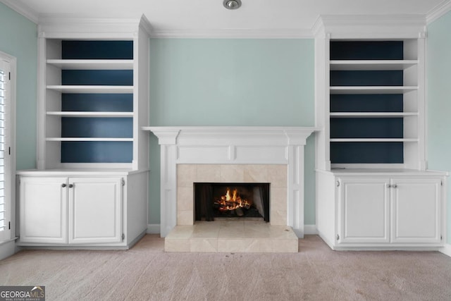 unfurnished living room with a tiled fireplace, built in features, light colored carpet, and crown molding