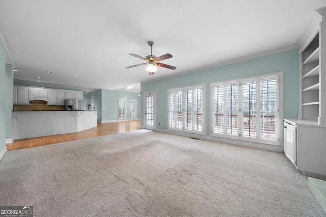 unfurnished living room featuring light colored carpet, baseboards, crown molding, and a ceiling fan